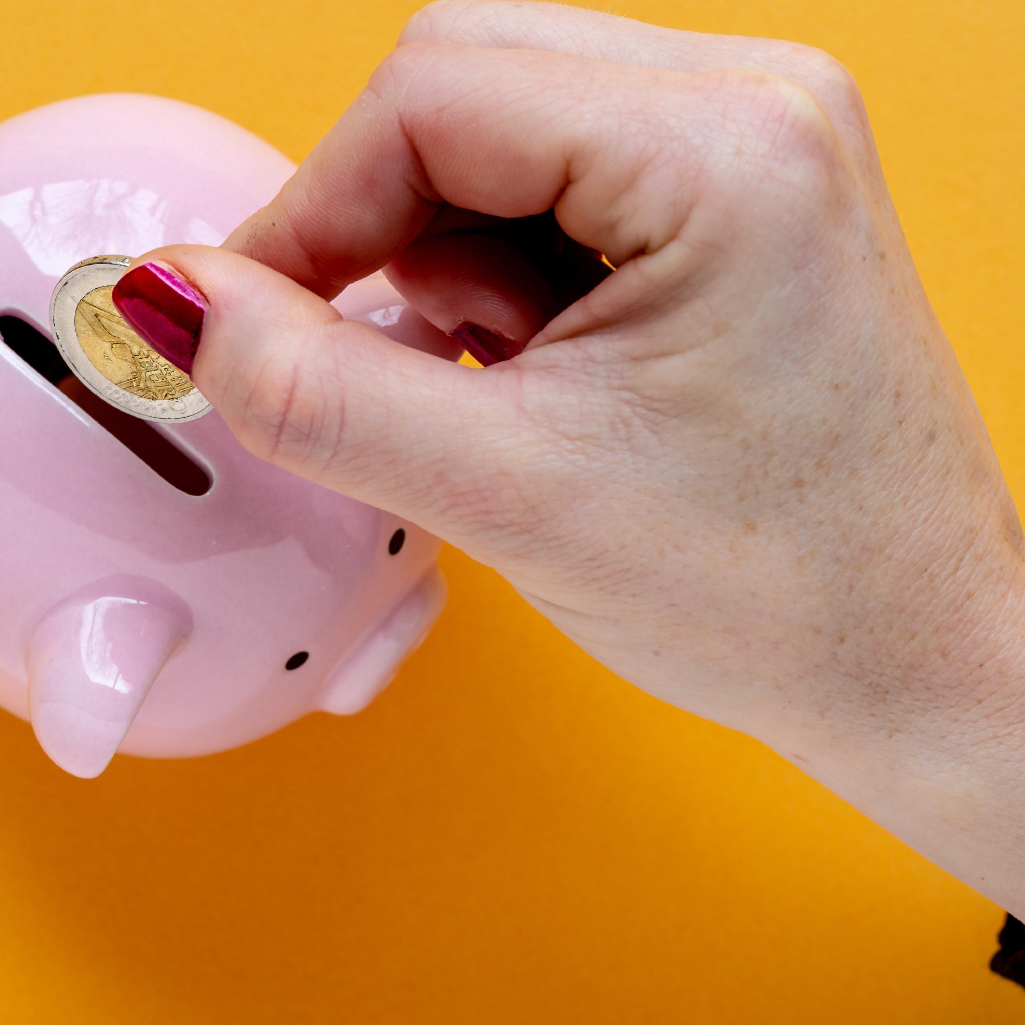 close up of woman putting money in a piggy bank on yellow background